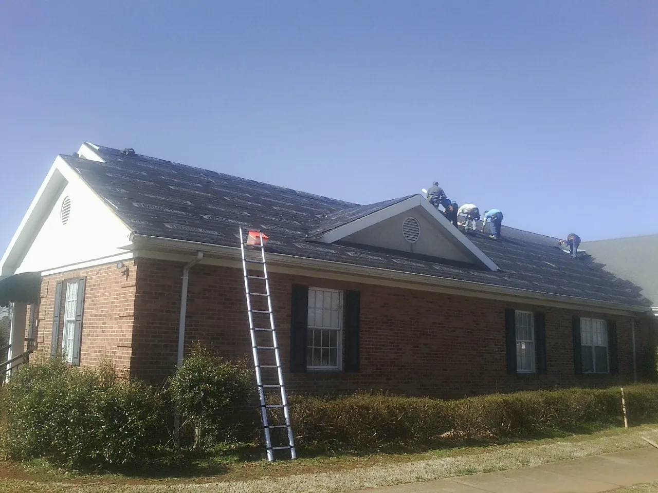 Crew tearing shingles off a brick ranch roof with a ladder set — Emergency Roof Repair work by our crew in Allenwood