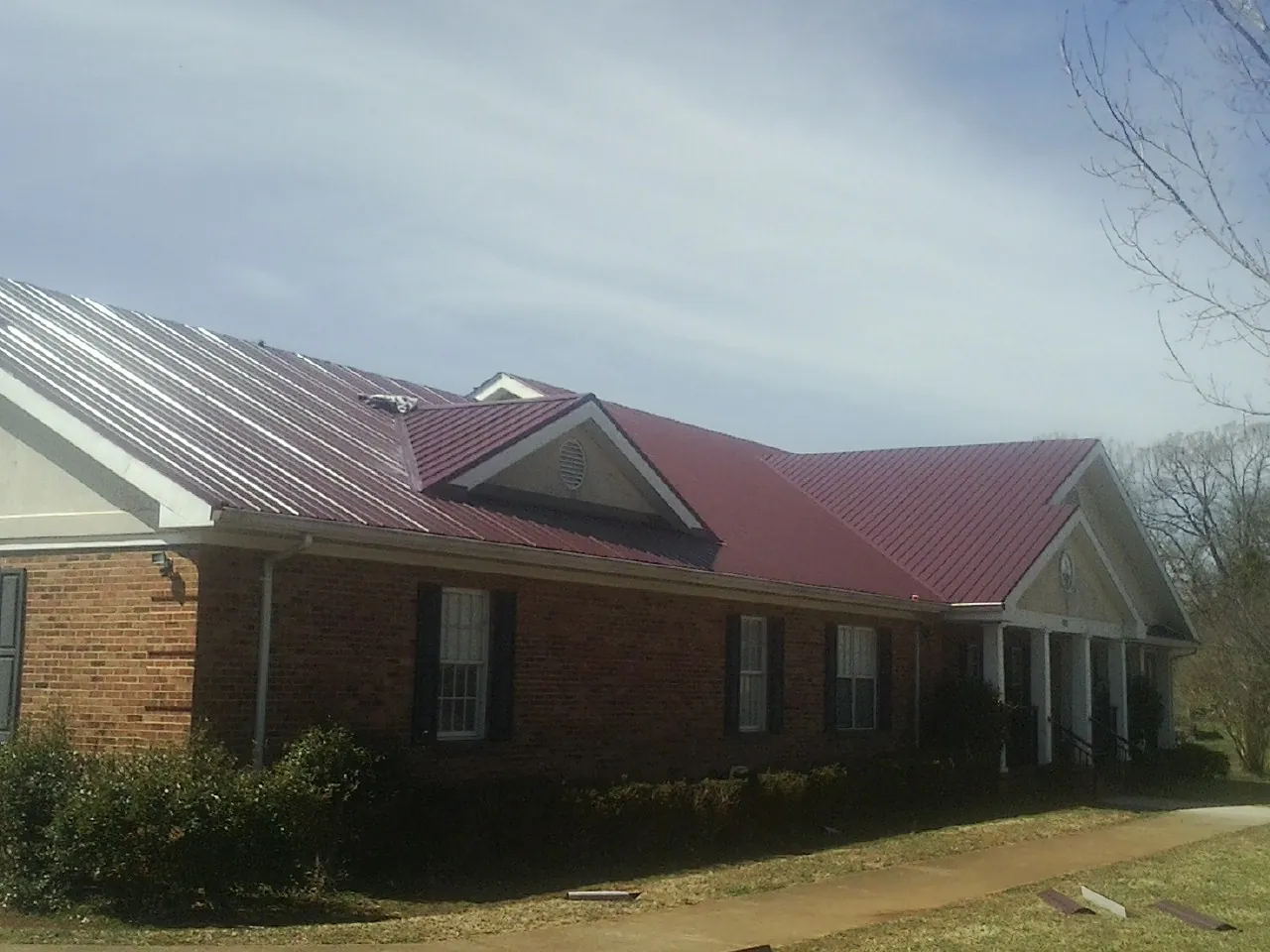 Red metal roof with gabled entries on a long brick building, from a Hail Damage Roof Repair job in Allenwood