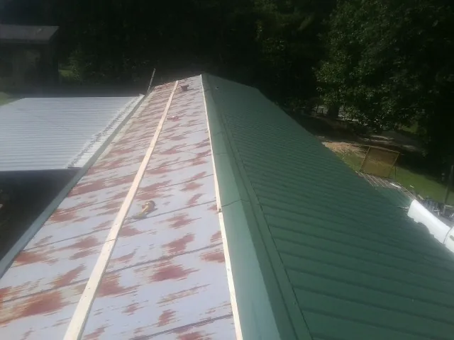 Old rusted panels beside newly installed green metal roofing — Wind Damage Roof Repair by Roofing Brothers in Allenwood