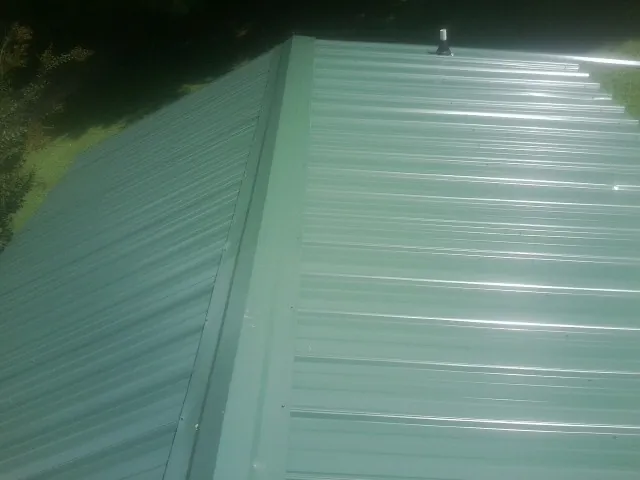 New green metal panels meeting at the ridge of a roof — Flat Roof Repair work by our crew in Allenwood