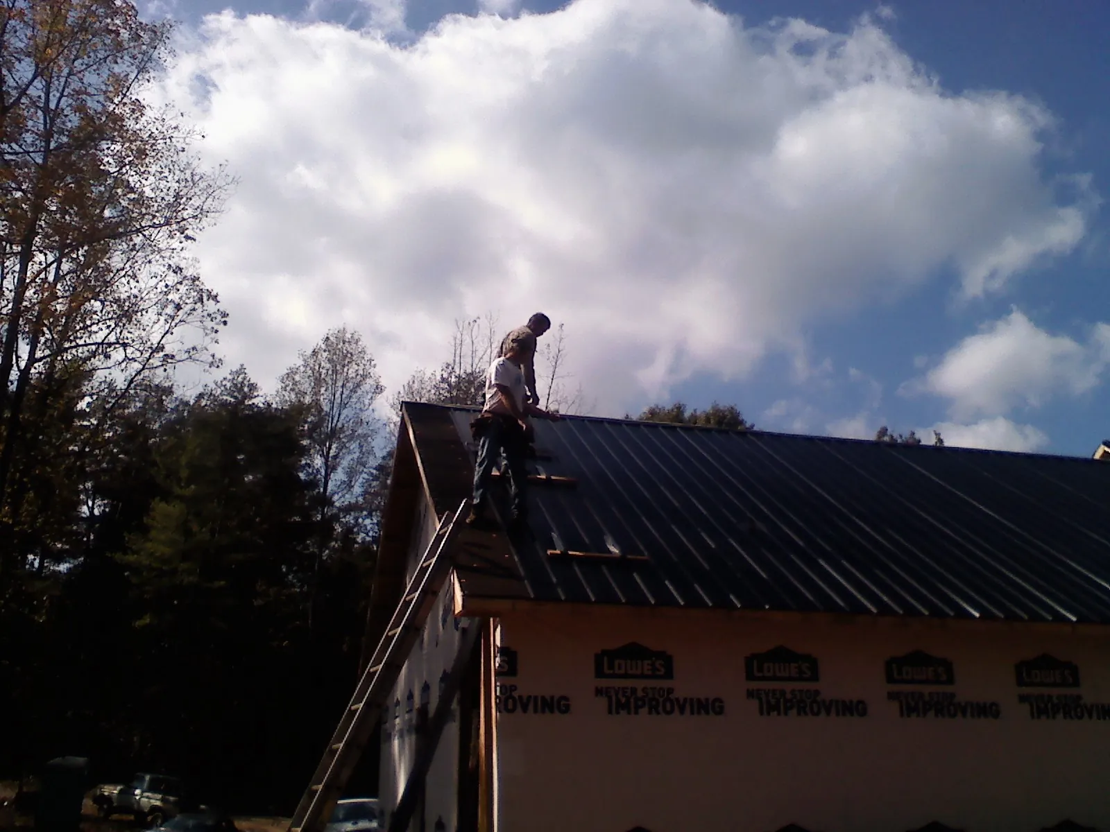 Roofer fastening dark metal panels high against a cloudy sky, from a Roof Inspection job in Allenwood