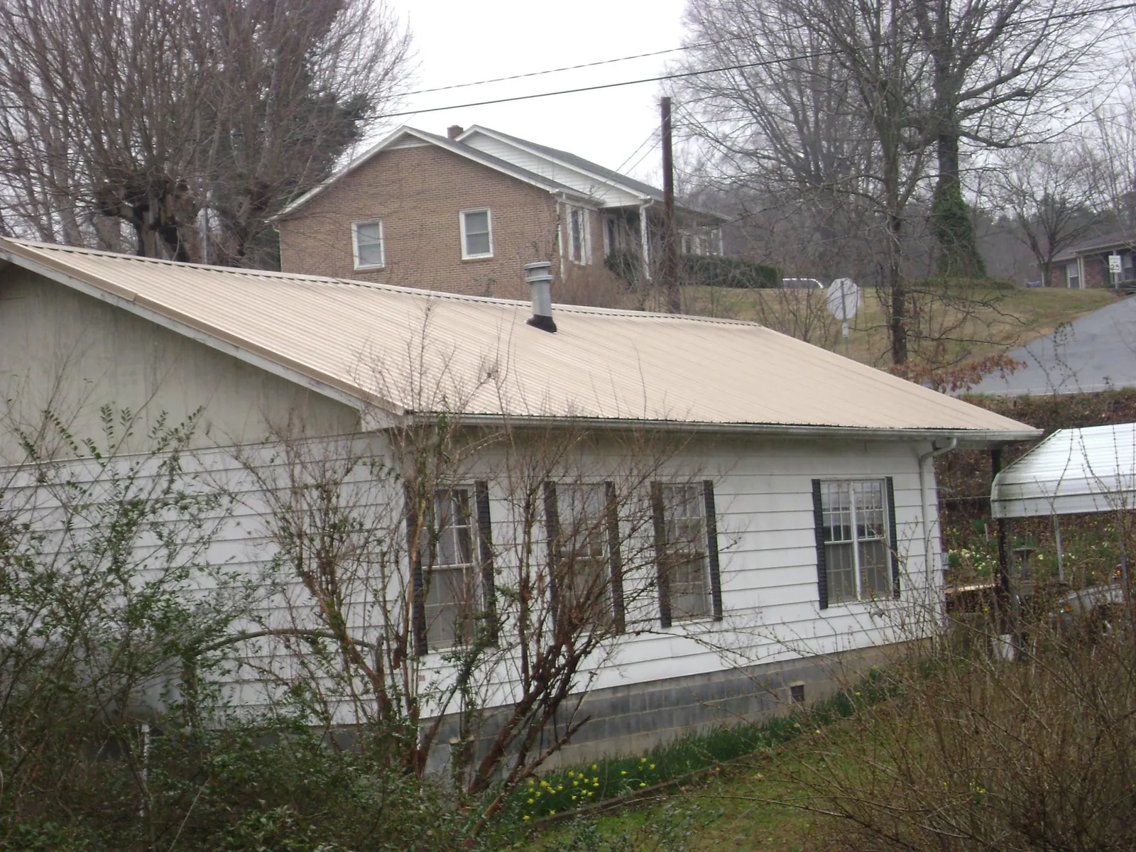 Tan metal roof on a white sided house set into a hillside — Commercial Roofing by Roofing Brothers in Allenwood
